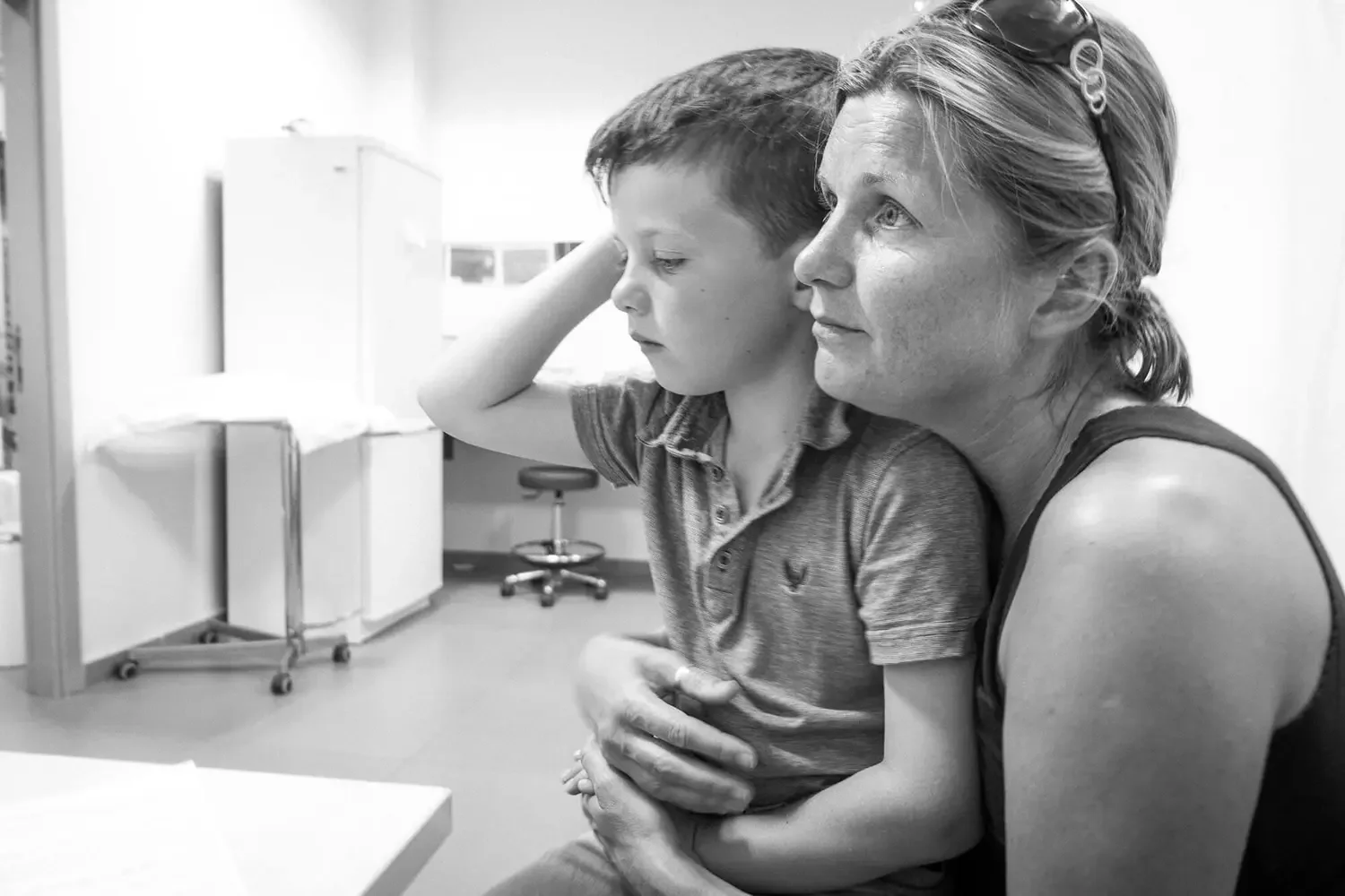 A woman holding a young boy in a medical setting, likely a doctor's office or hospital room.