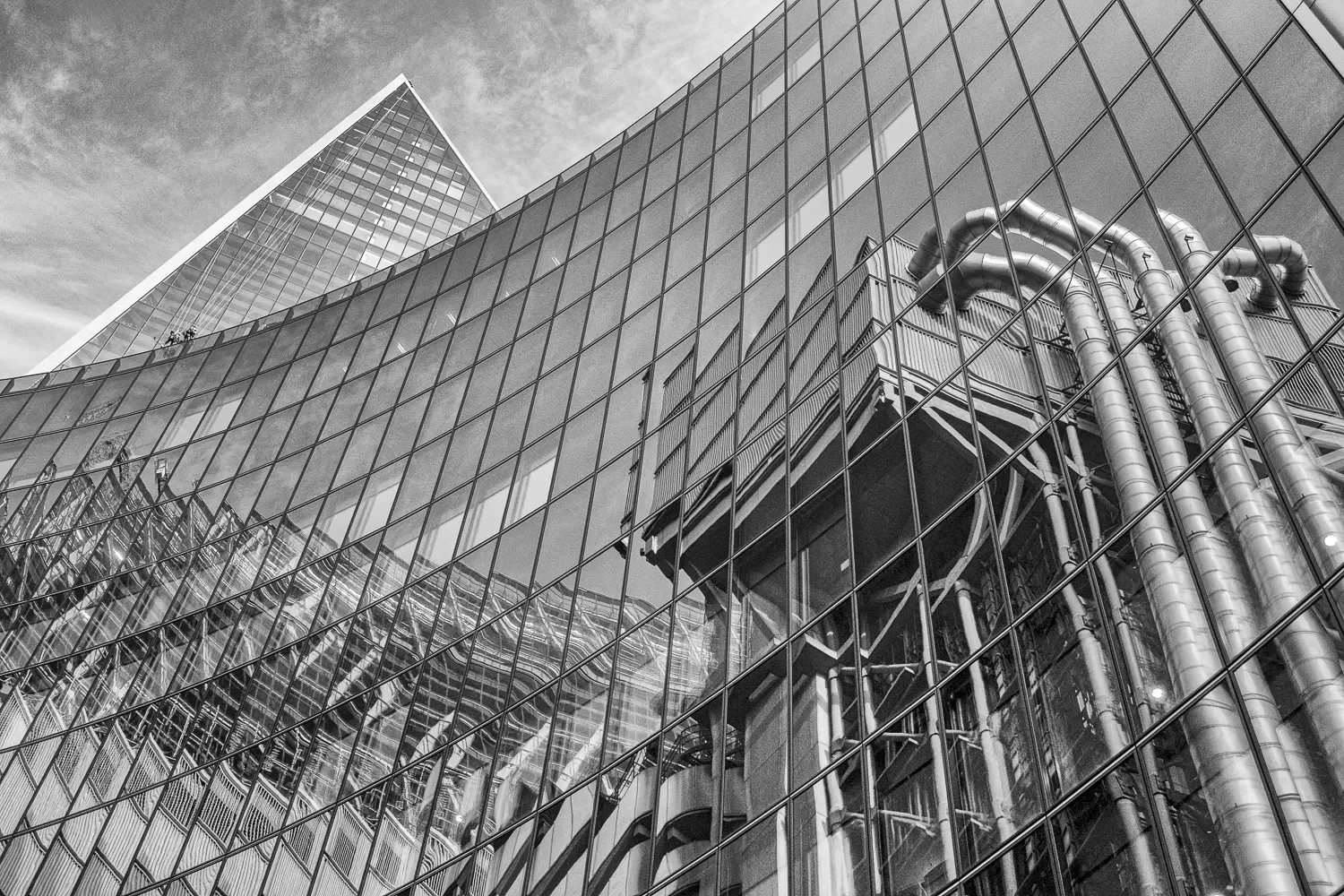 The steel pipes and ducts of Lloyd's of London reflected and refracted in the curved glass facade of an adjacent tower, black and white