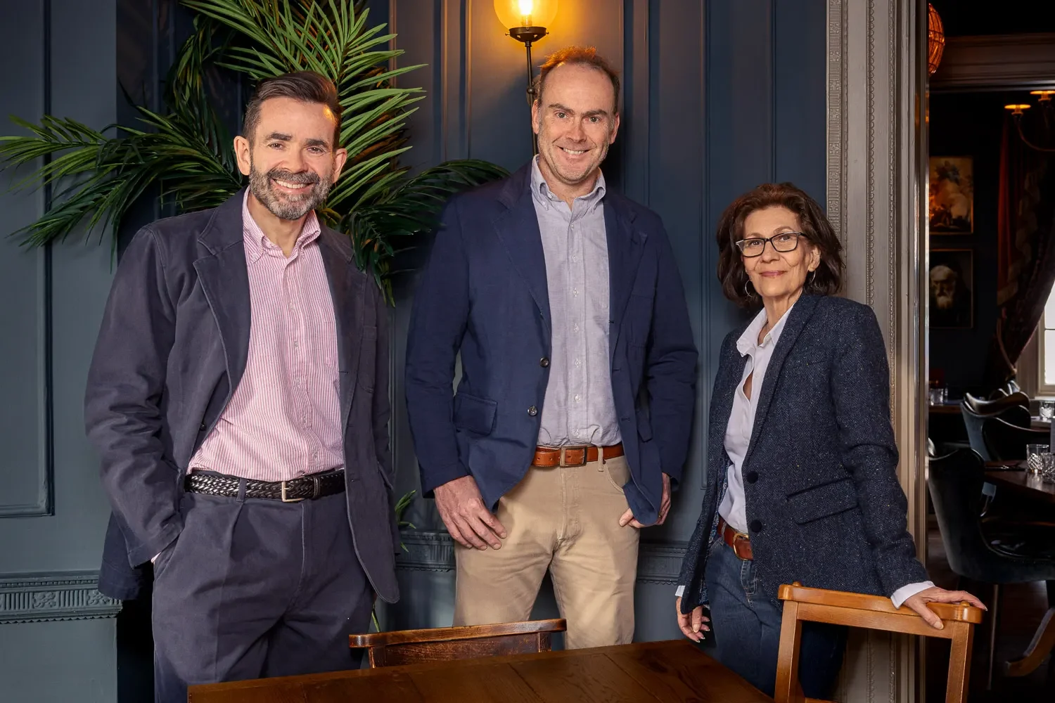 Three colleagues standing together in a blue panelled room with warm wall lighting — professional corporate headshots taken on location at a St Albans pub