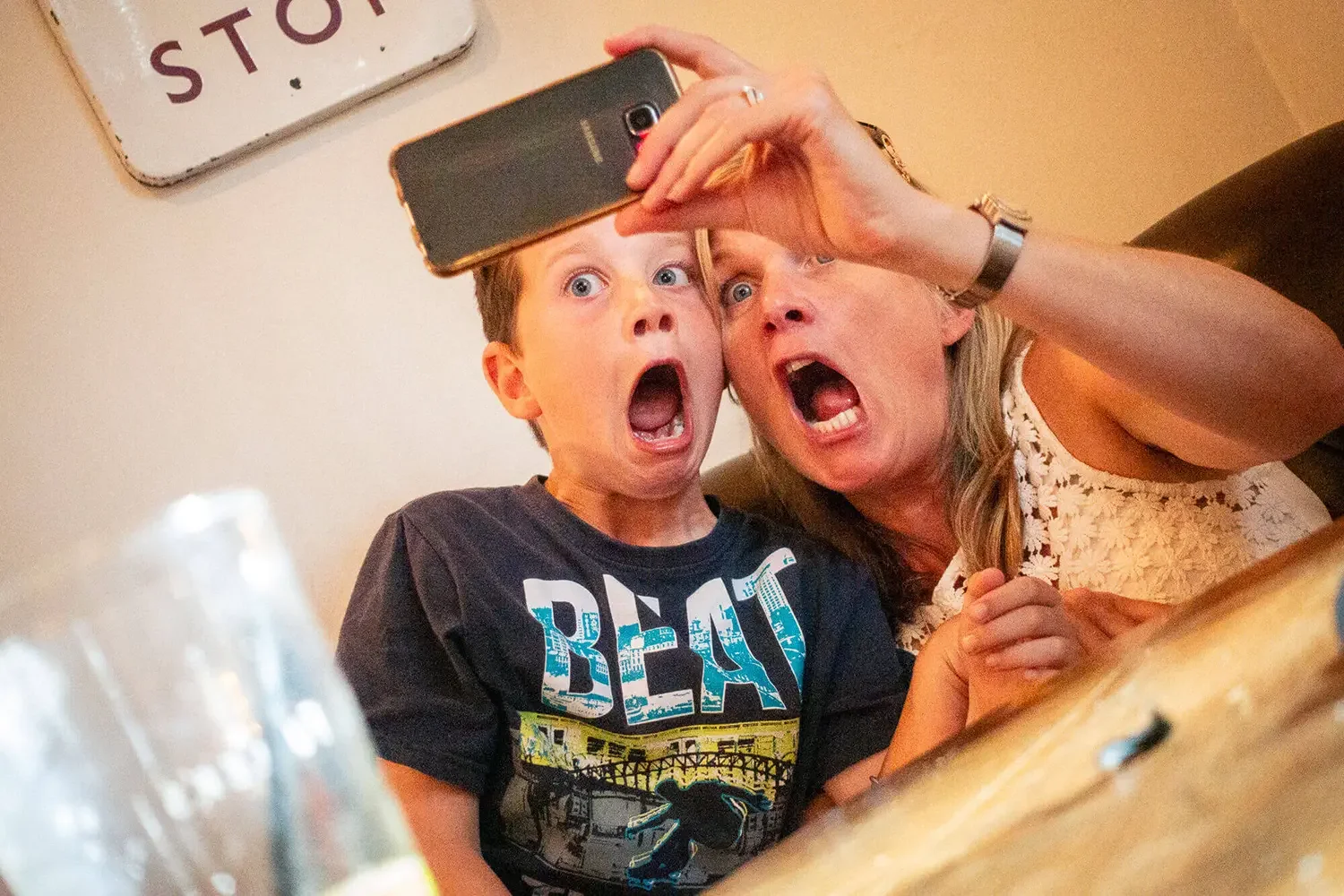 A woman and a boy taking a selfie together, both with surprised or shocked expressions, in a casual indoor setting.