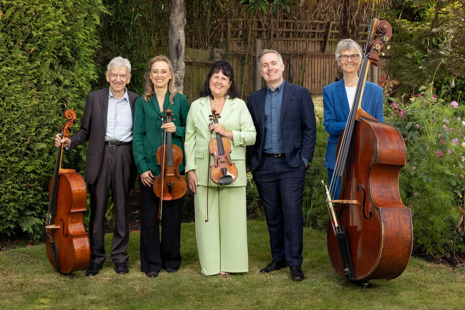 Classical music quintet with cello, viola, violin and double bass posing in a garden in Arkley, Barnet, photographed by Mike Dick Photography.