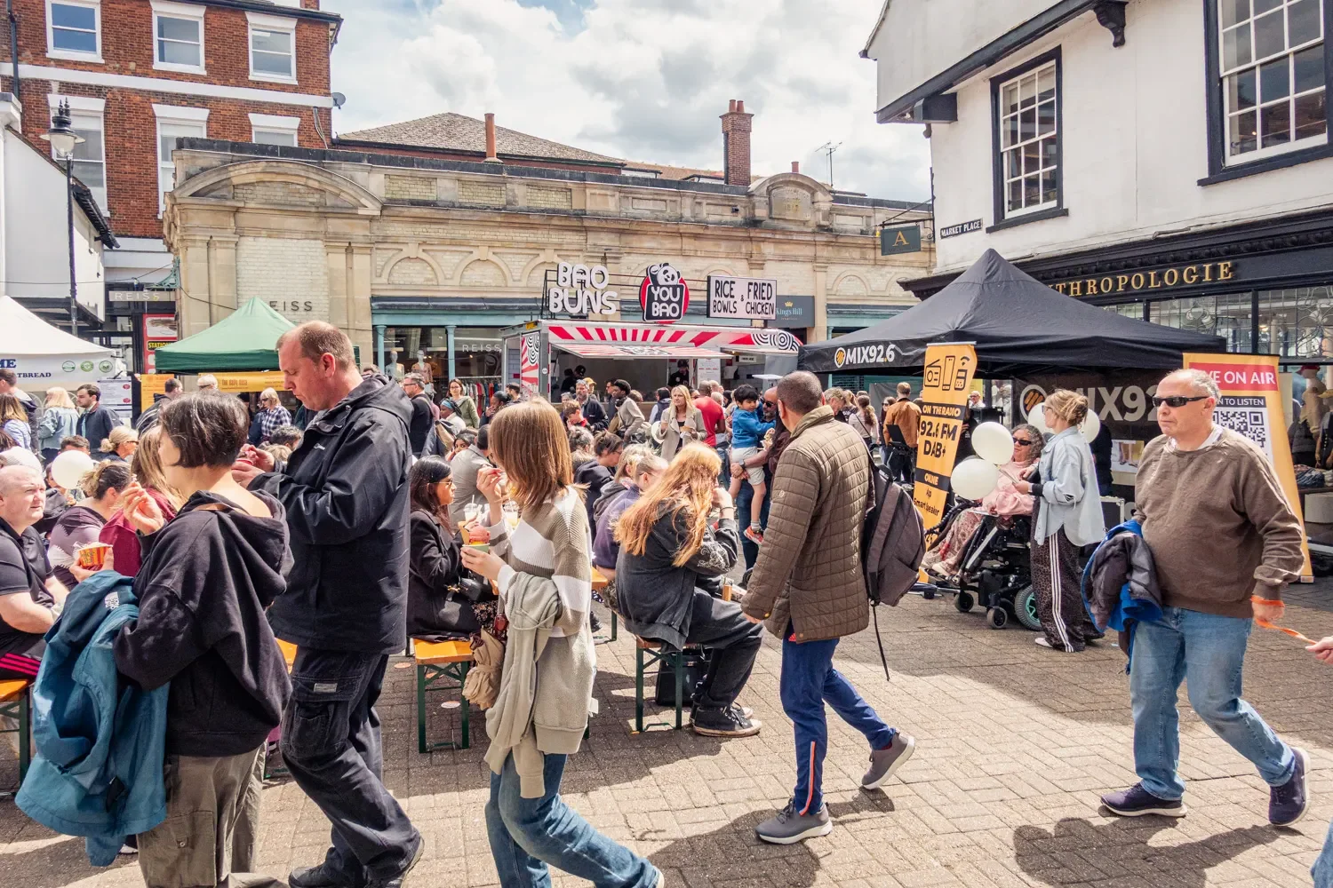 Busy St Albans market day with crowds of shoppers, street food stalls, and Mix 92.6 FM broadcasting live from the town centre