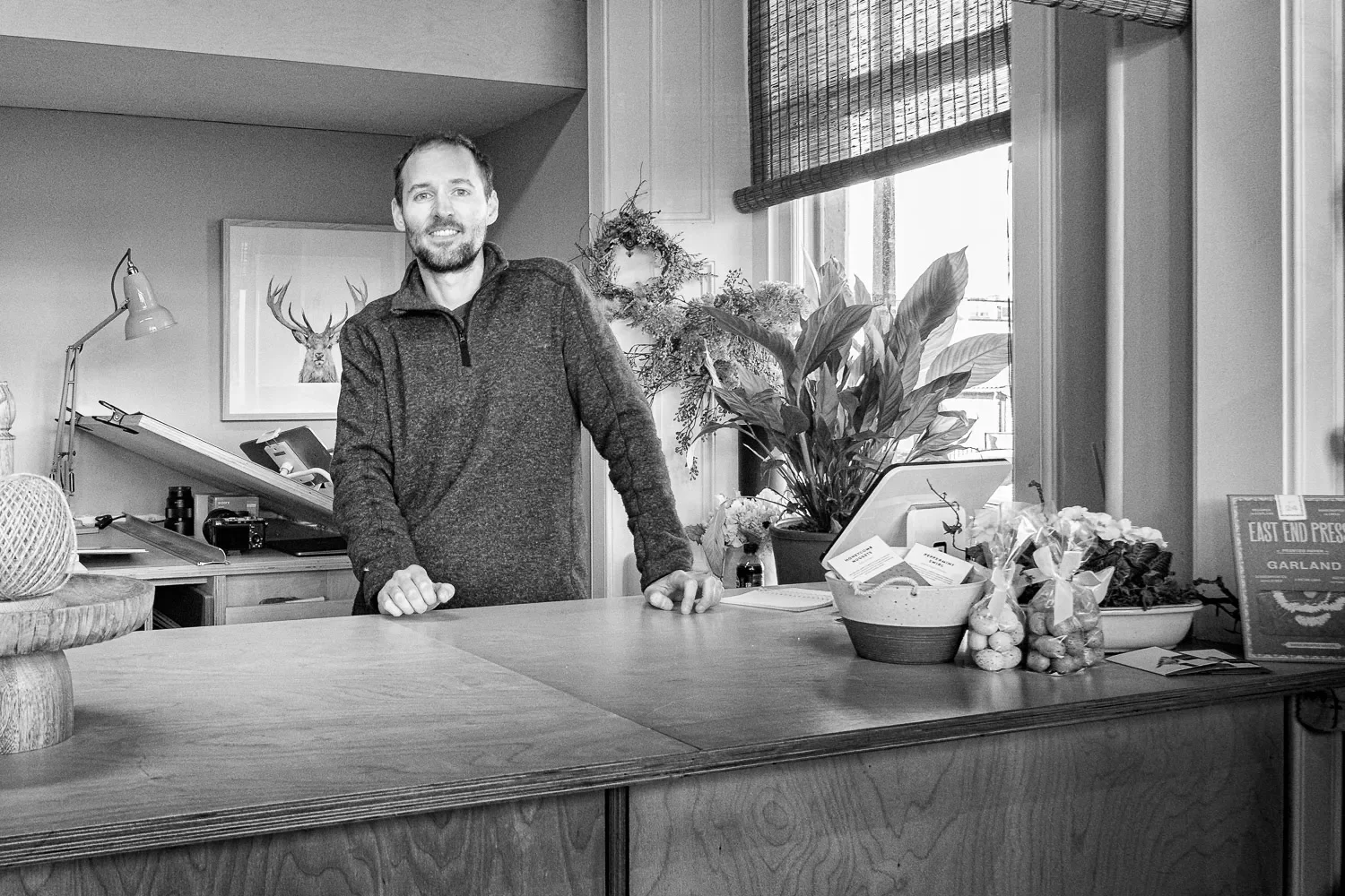 Stuart Scott standing behind the counter at Sasco Art gallery, Helensburgh, black and white environmental portrait