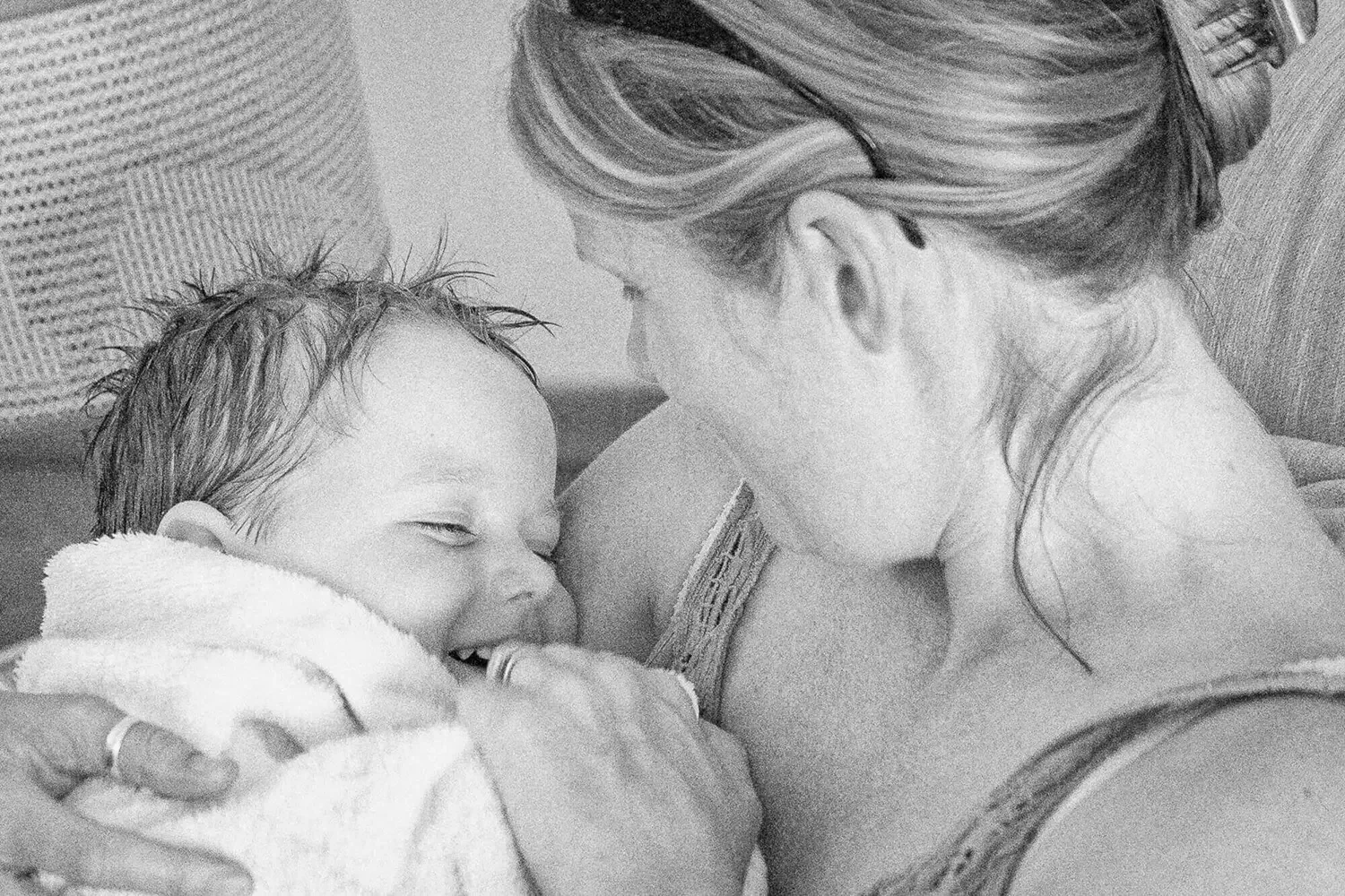 A woman and a smiling baby sharing a close moment, with the woman lying down and the baby on her chest, both appearing happy and affectionate.
