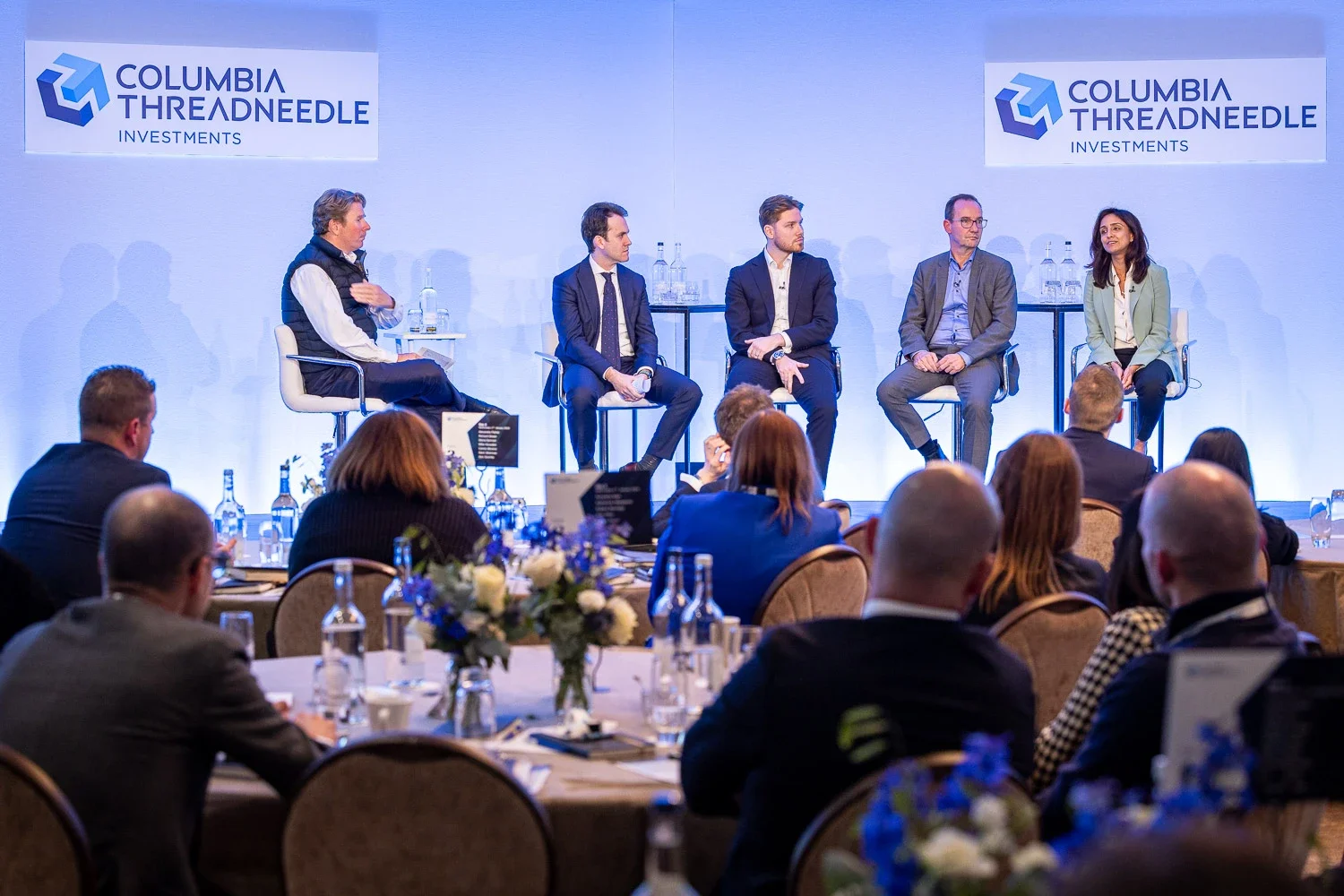 Five-person panel discussion on stage at a corporate investment conference in London