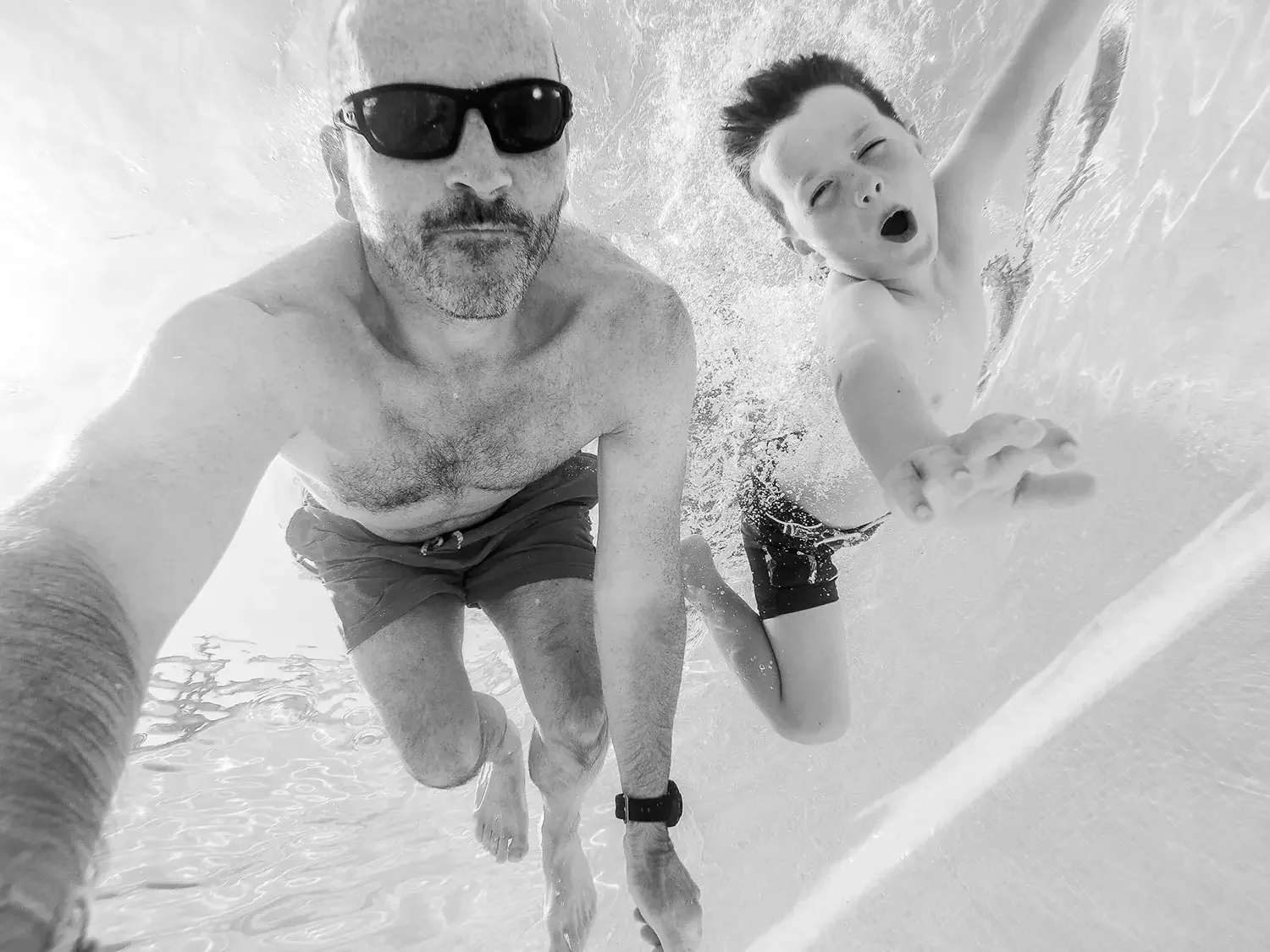 Young boy and dad dive under the water in a swimming pool.