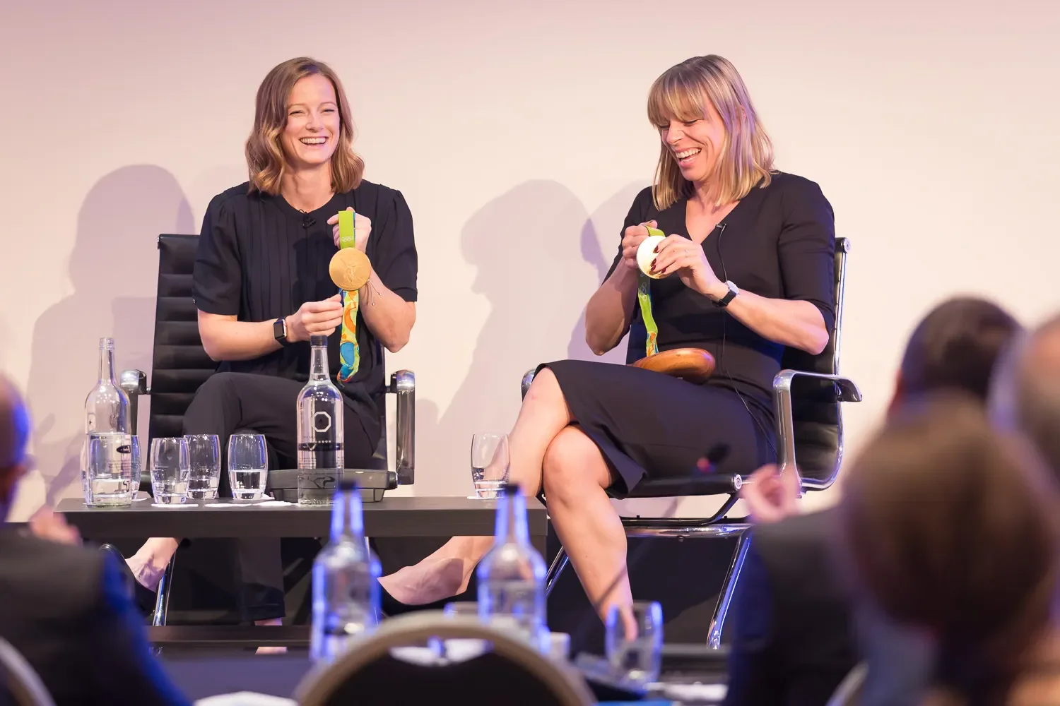 Two Olympic gold medallists holding their medals and laughing during a panel discussion at a corporate event in London
