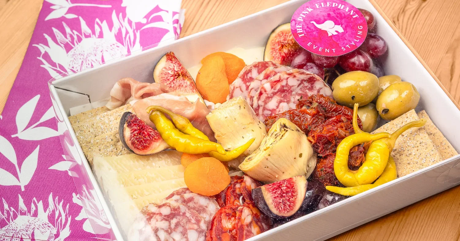 The Pink Elephant charcuterie box in pink packaging — figs, cheese, salami, peppers and olives, food photography St Albans