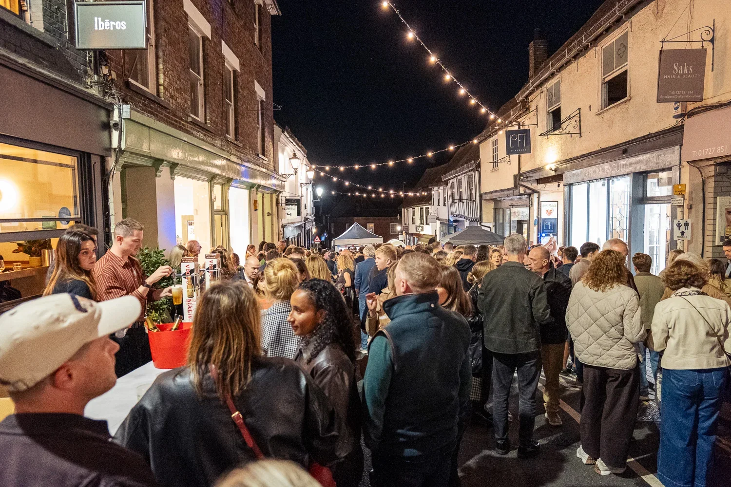 Crowds packing George Street at night under strings of festoon lights, with Tudor buildings on either side