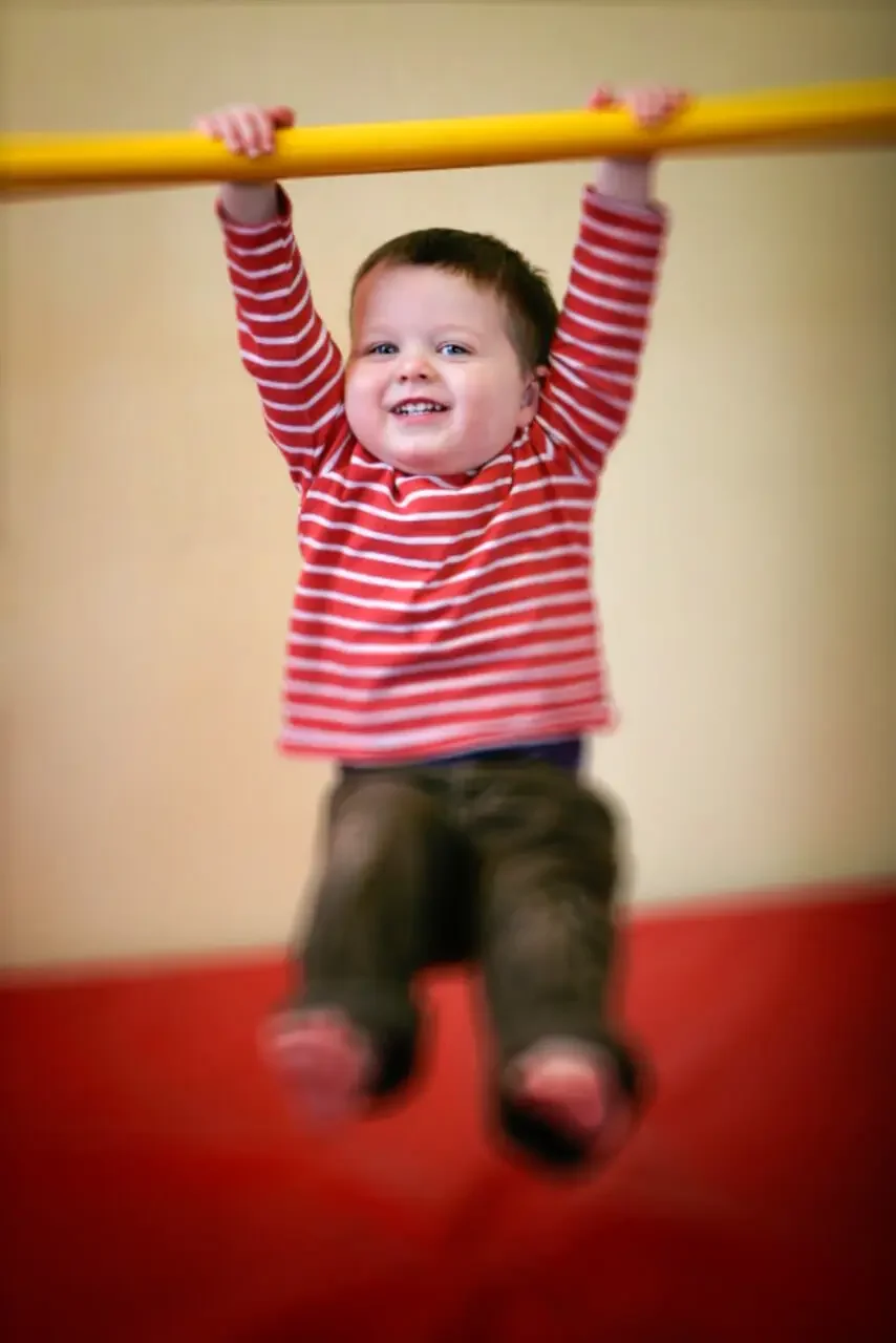 Young boy swinging from a bar at a gym.