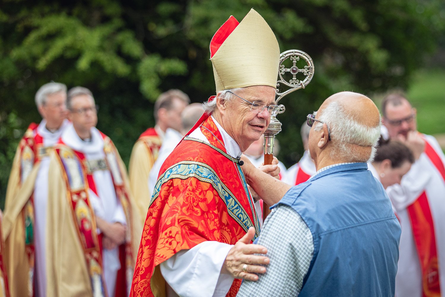 Bishop in red vestments and mitre greeting a pilgrim outside St Albans Cathedral during Alban Day 2026 pilgrimage, Hertfordshire.