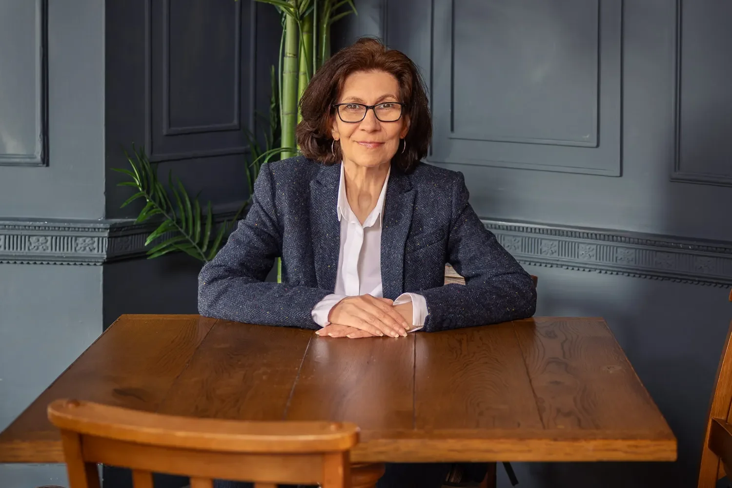 Female business professional in a tweed blazer seated at a wooden table in a blue panelled room — professional headshot photography, Hertfordshire