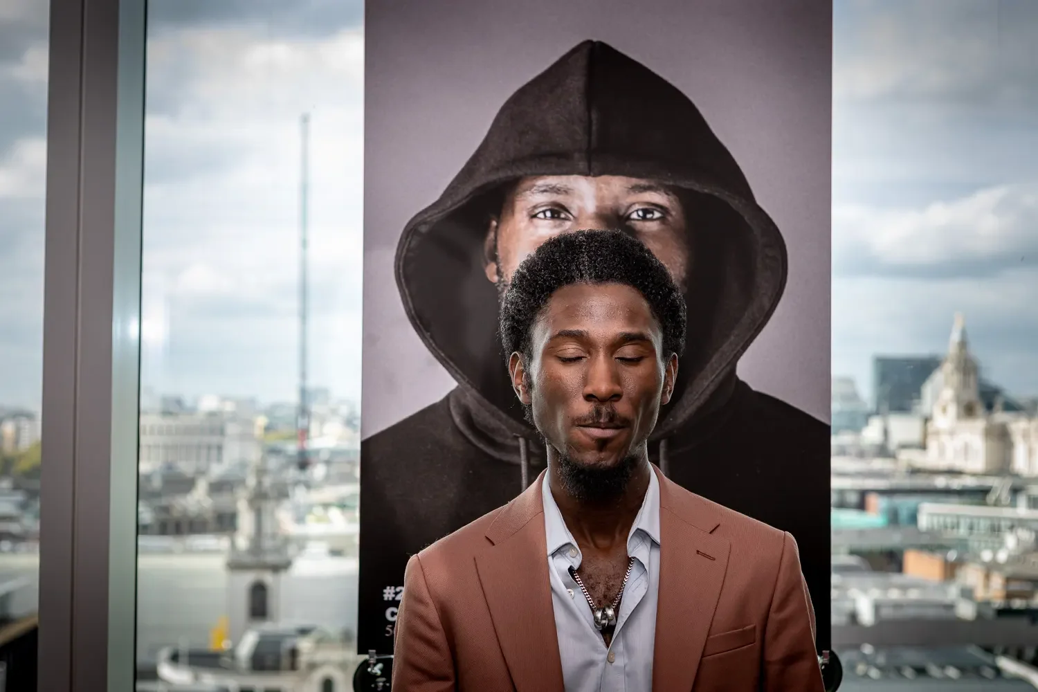 Portrait of a speaker at a corporate event in London with city skyline visible through floor-to-ceiling windows.