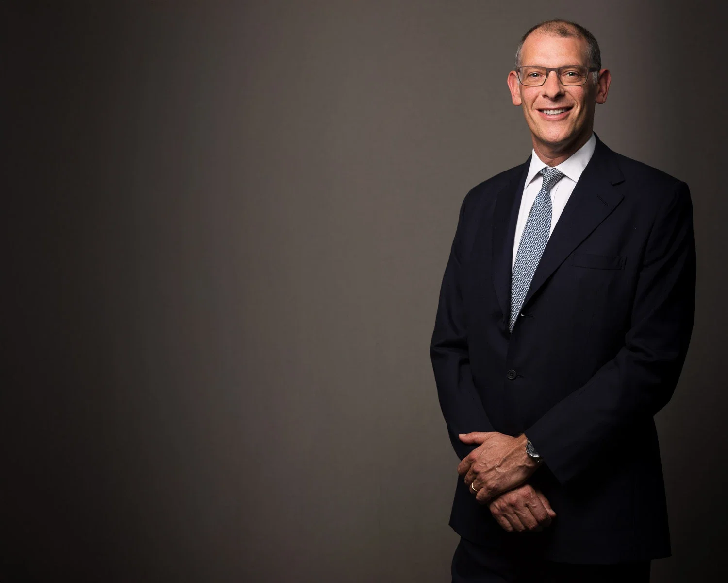Smiling executive in a dark suit, lit against a dark grey studio backdrop, London
