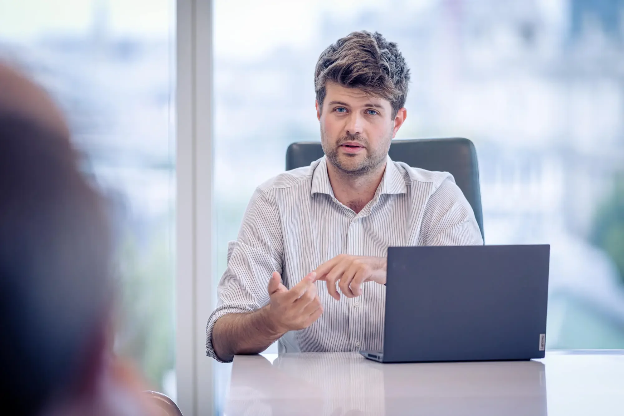 Man in a striped shirt speaking during a business meeting in an office.