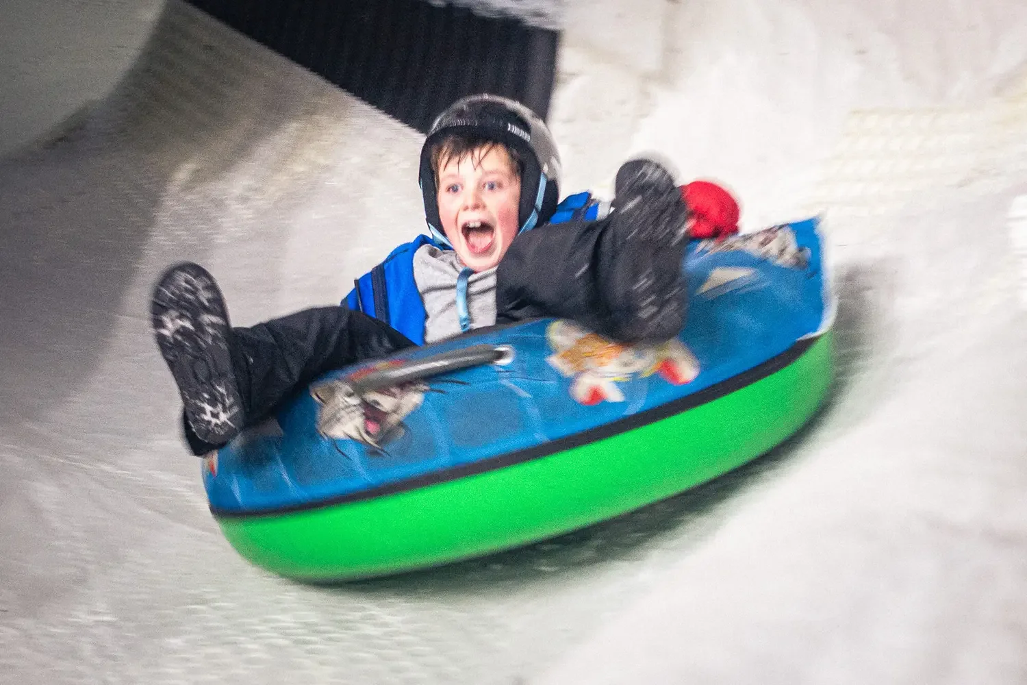 Young boy on rubber ring goes down a snow slide.