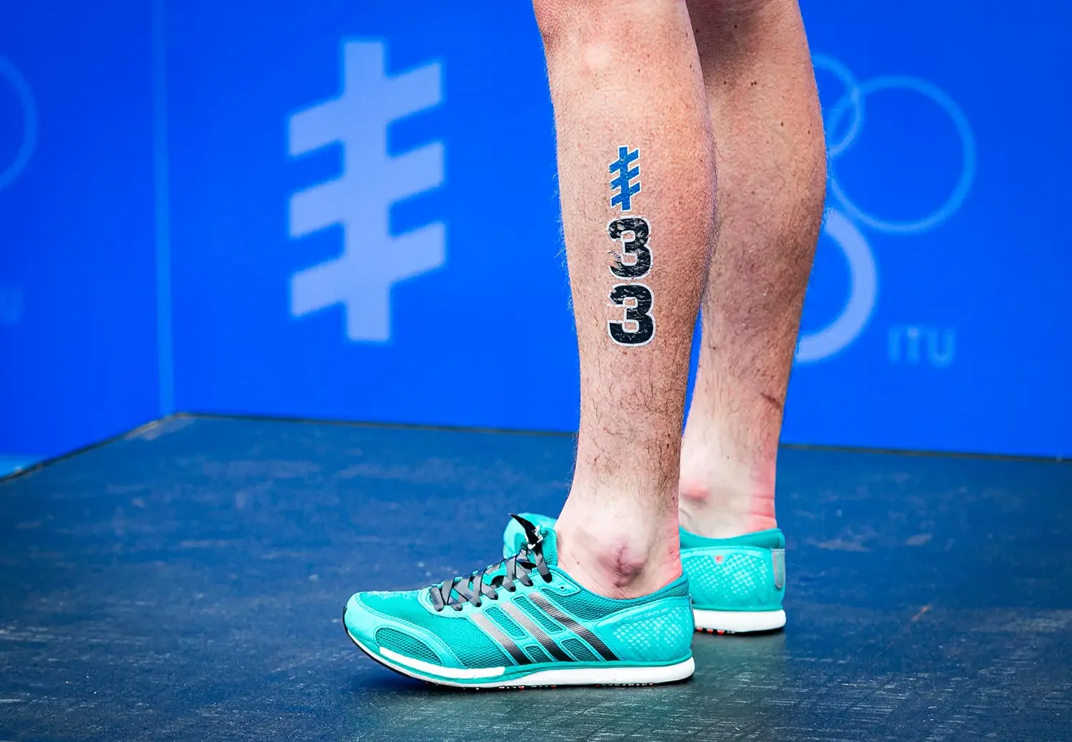 A close up of a triathletes leg with his race number stenciled on his calf.