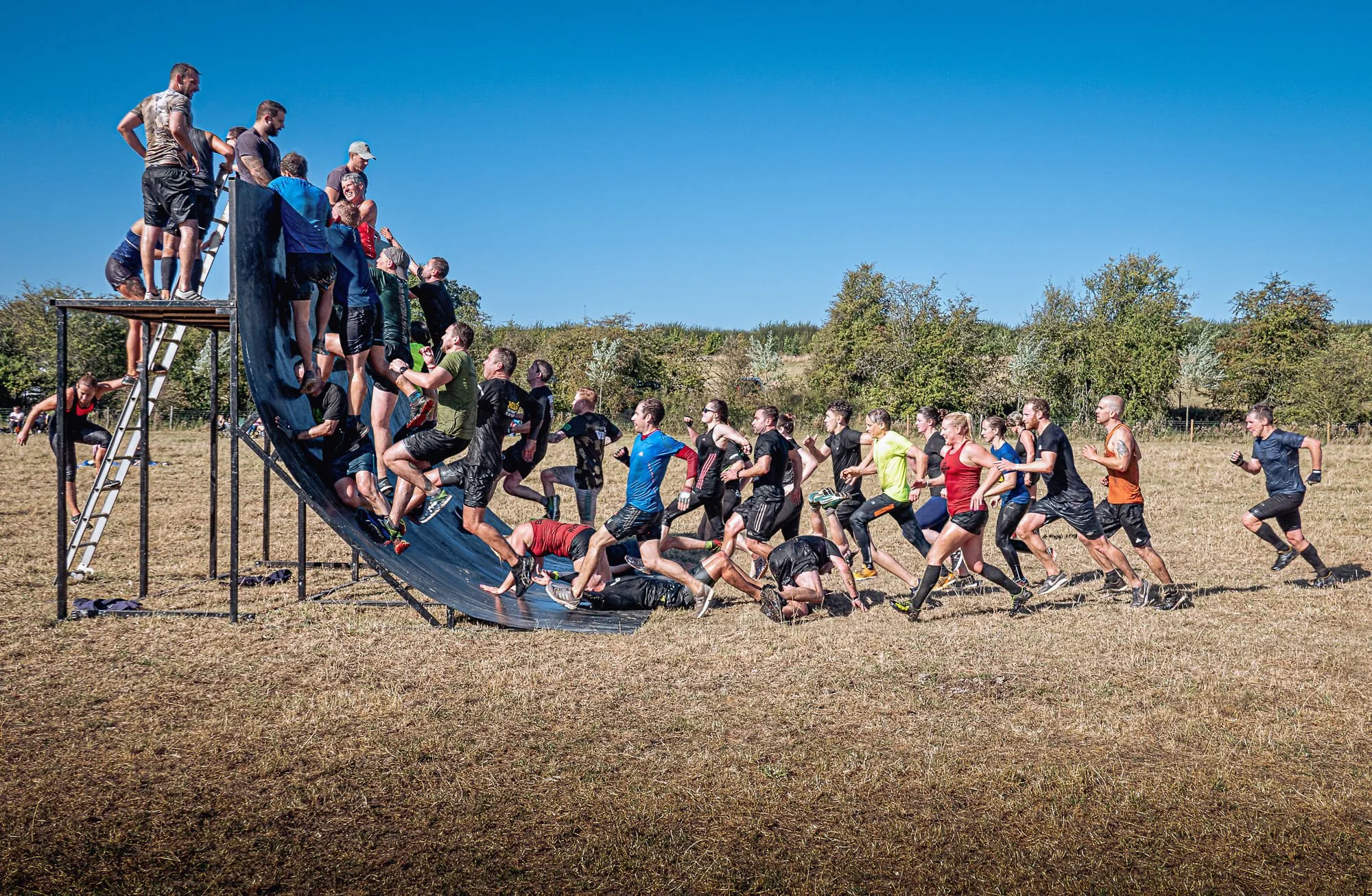 Competitors climbing and sliding down a wall obstacle in Hertfordshire