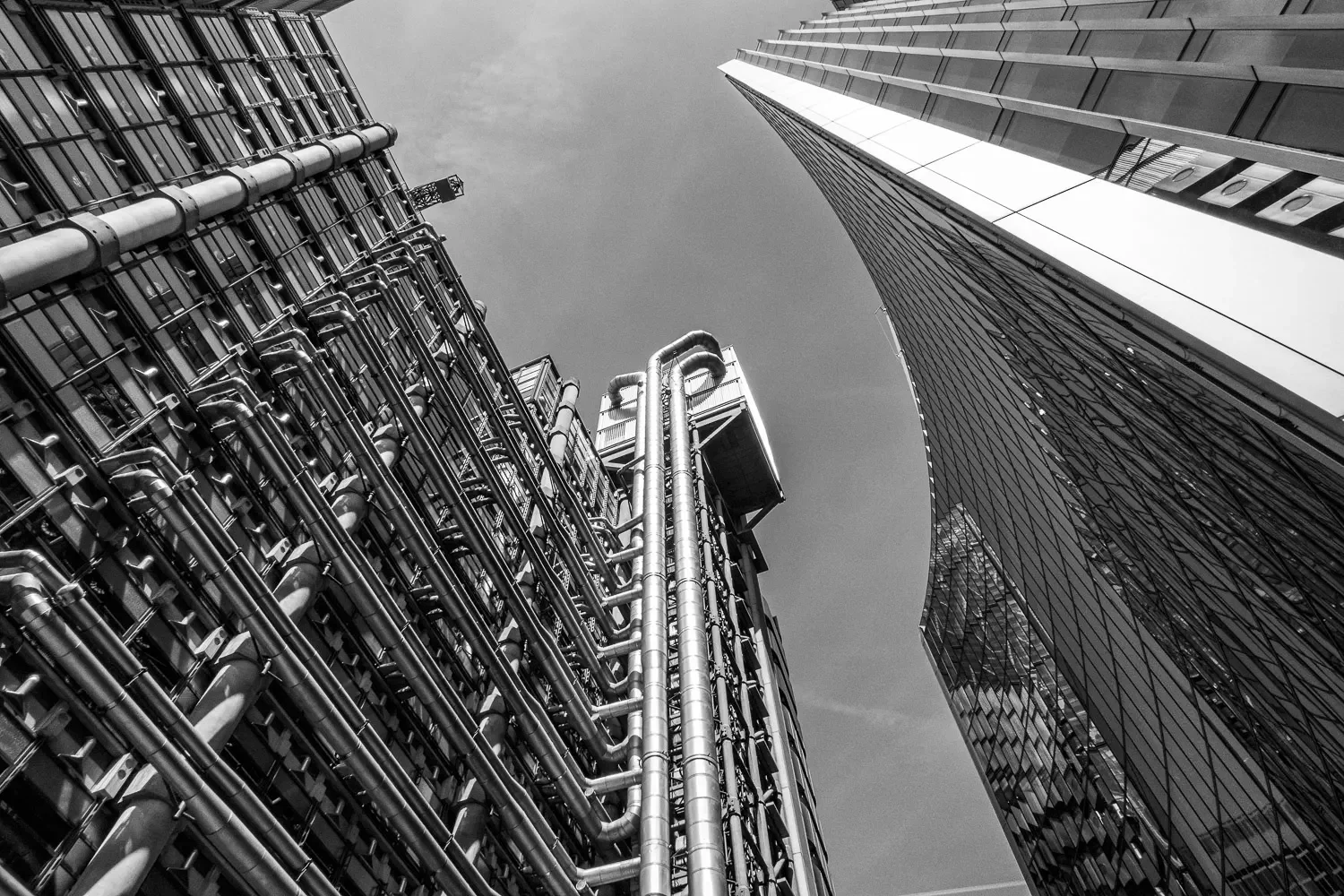 Lloyd's of London and a neighbouring glass skyscraper rising above a narrow City street, viewed from ground level, black and white portrait
