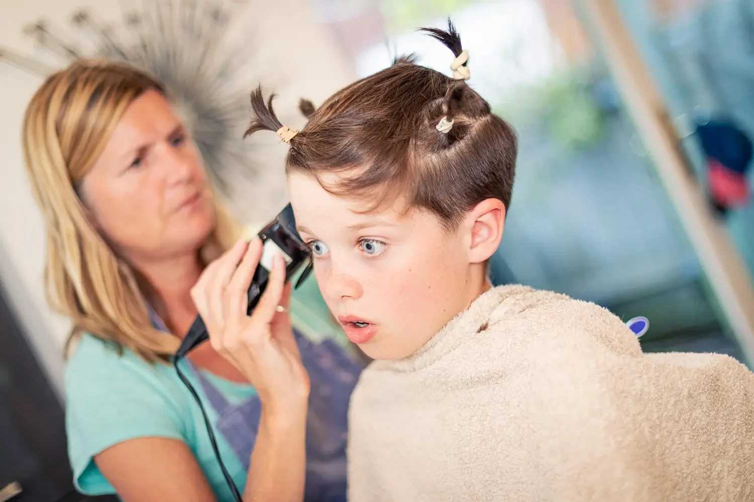 A small boy not happy haveng his hair shaved by his mum at home.