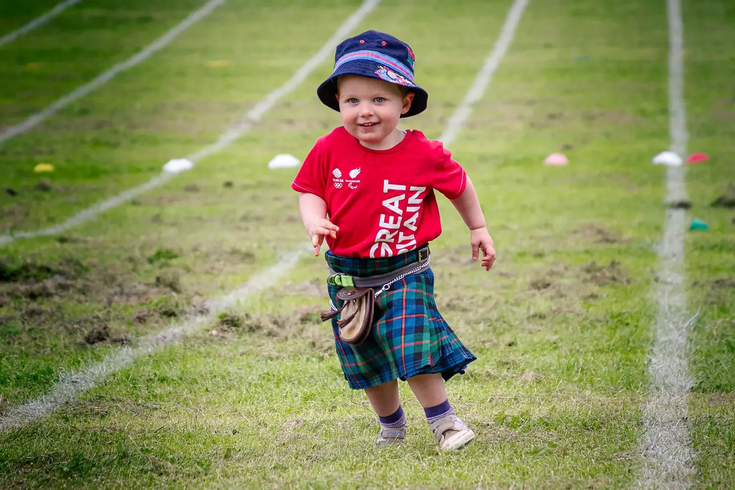 Young boy wearing a kilt running on a field running track.