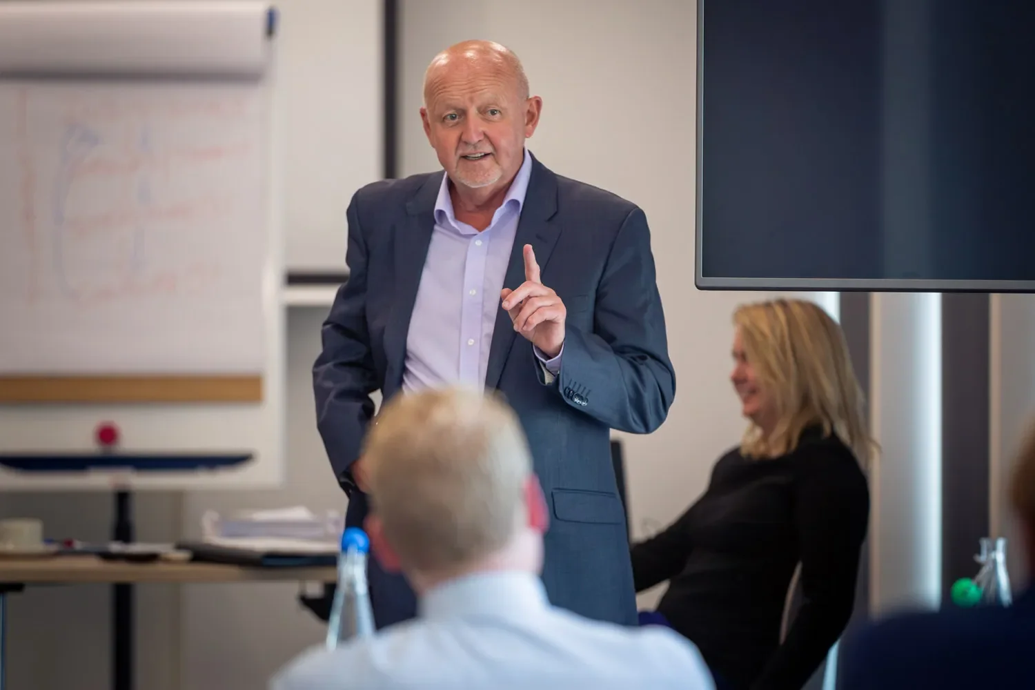 A man in a suit stands in front of a group of people, giving a presentation at a corporate event in London.