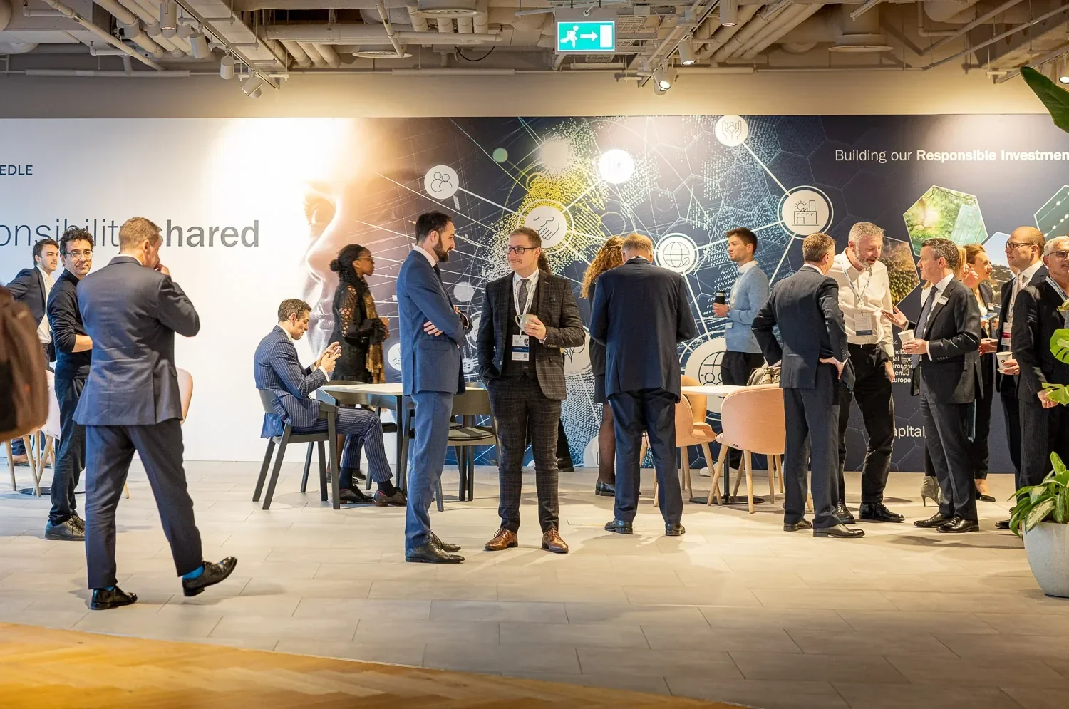 Guests networking at a corporate event in a London office, in front of a branded wall