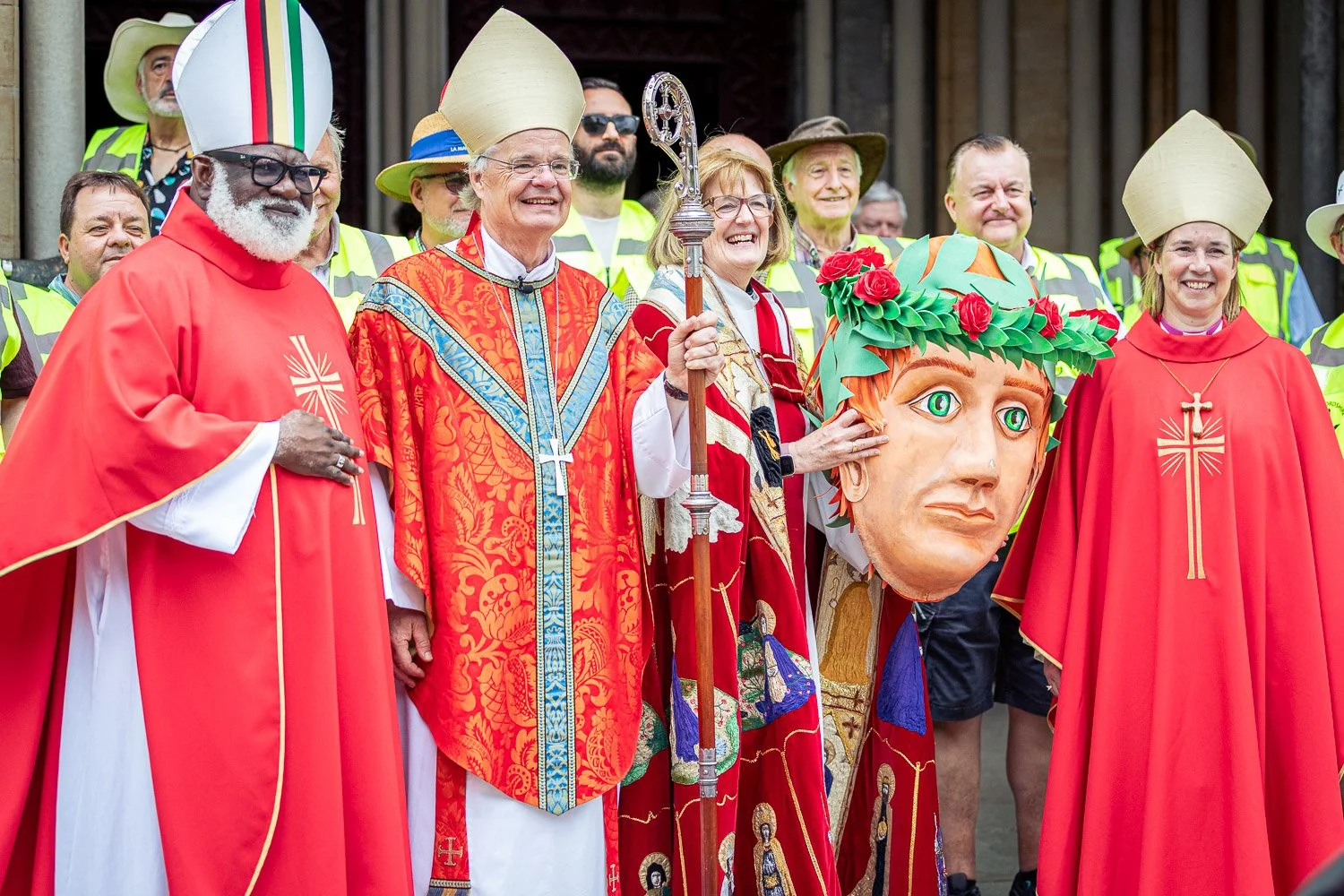Four bishops in red vestments posing with a large Saint Alban puppet on the steps of St Albans Cathedral, Hertfordshire, during Alban Day 2026