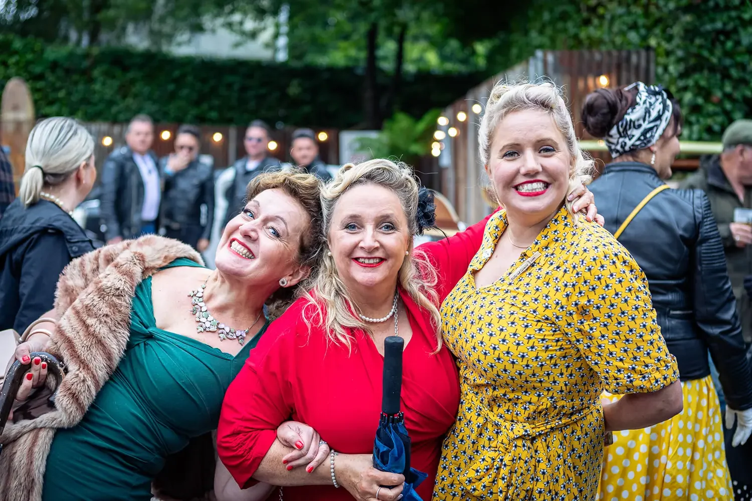 Three ladies dressed in 1940s costumes pose for the camera at the Goodwood Revival event.