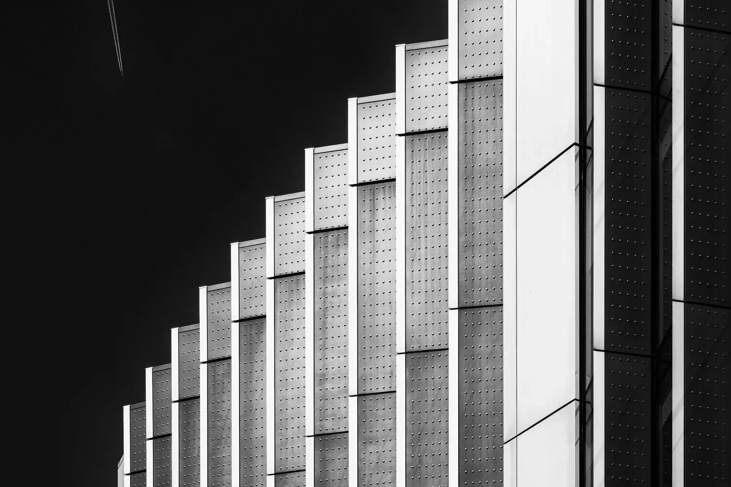 Abstract close-up of repeating stepped perforated metal cladding panels on a City of London building, high contrast black and white
