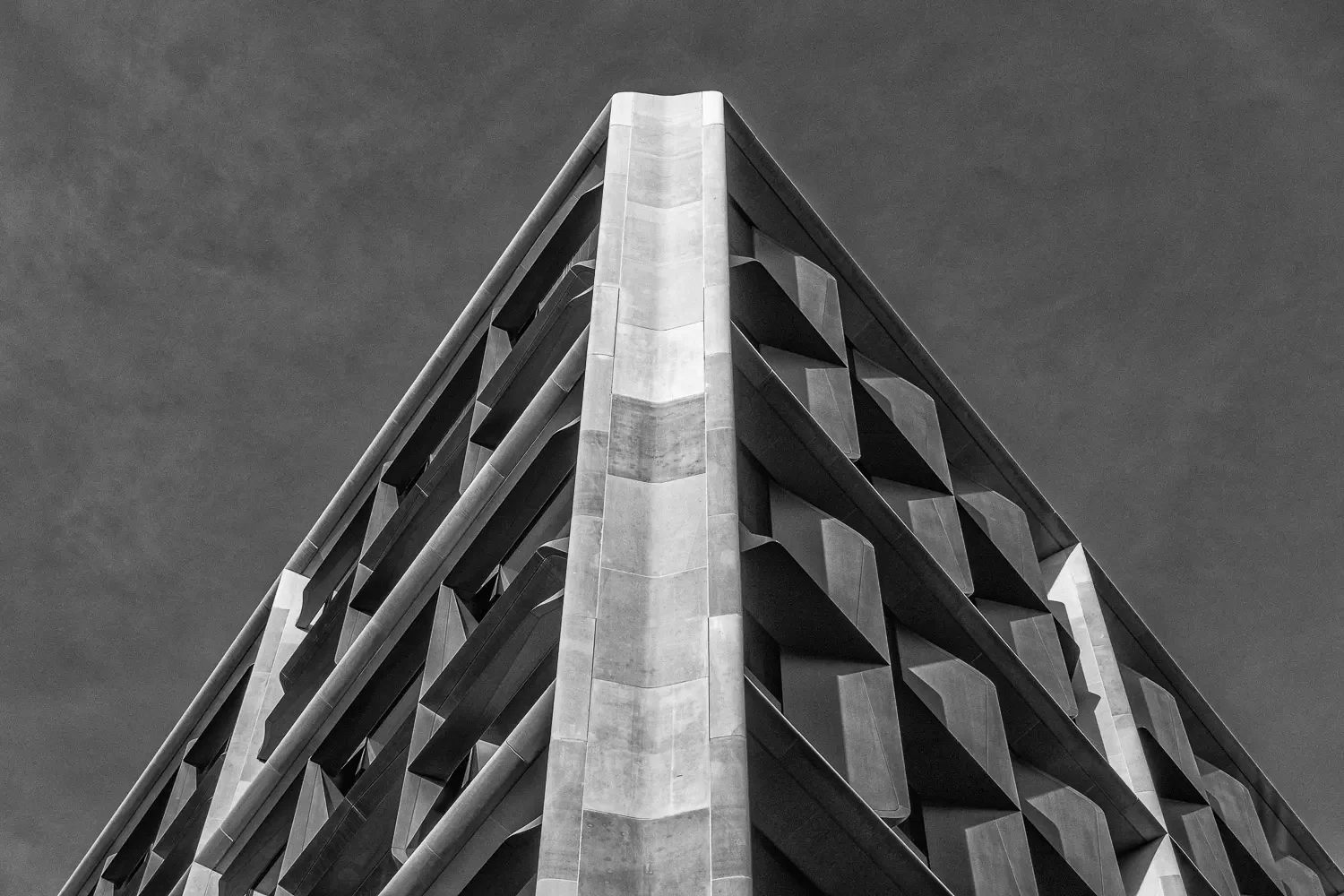 The sharp apex of a faceted stone-clad City of London tower against an overcast sky, geometric angular cladding in black and white