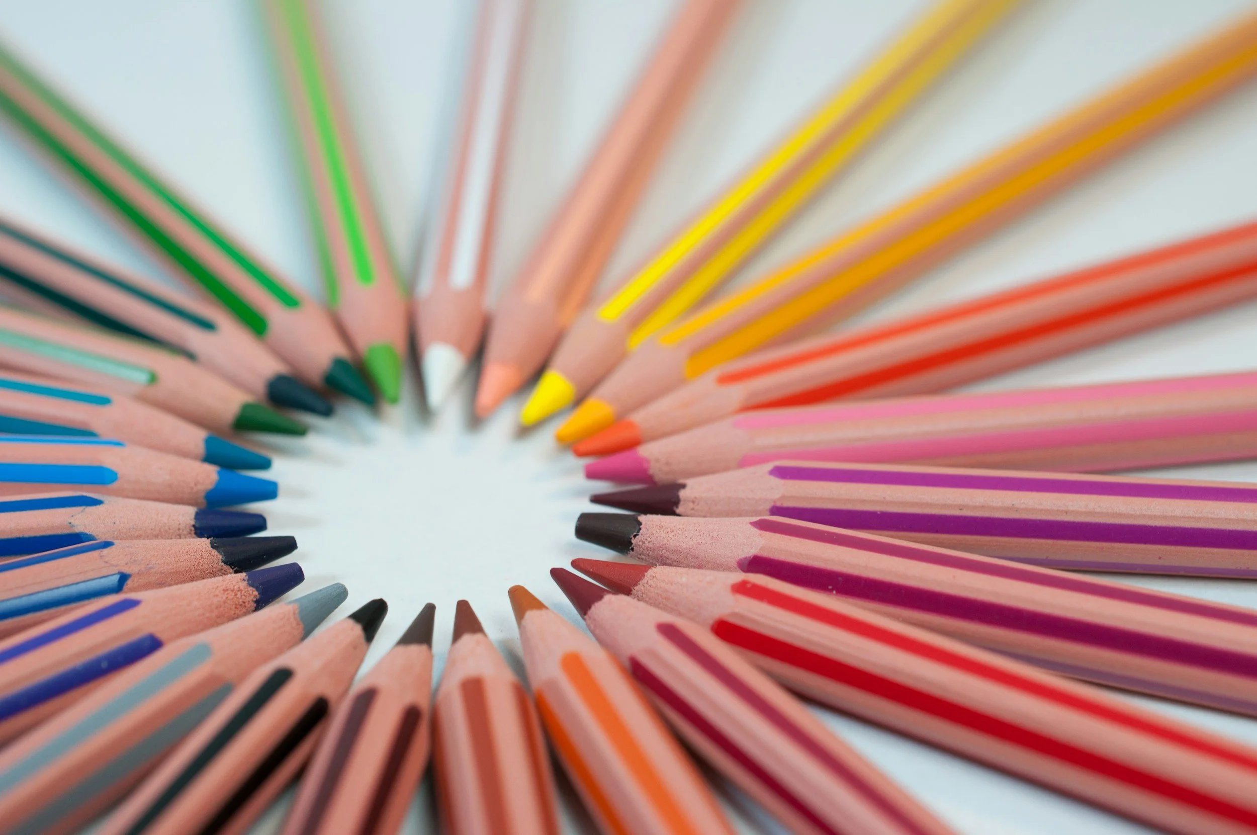 Colored pencils arranged in a circle, showcasing a variety of colors including green, yellow, pink, red, purple, blue, and black.