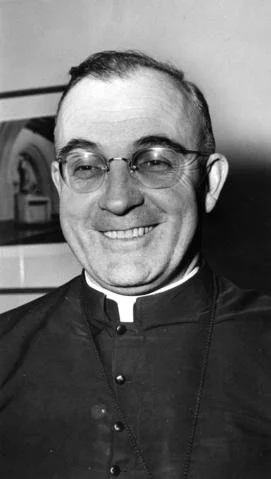 Black-and-white photo of a smiling man wearing glasses and a clerical collar.
