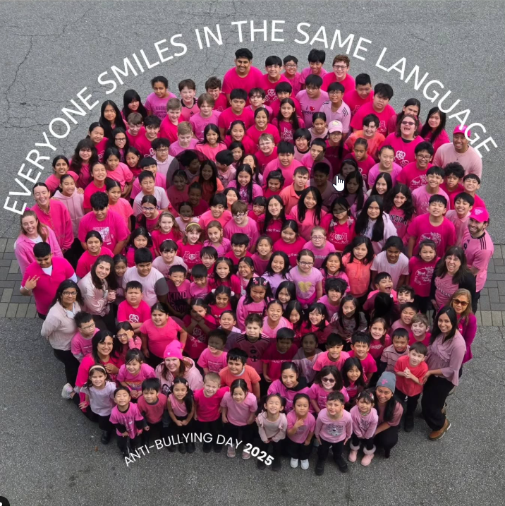 Large group of children and adults wearing pink shirts and standing in a circle outdoors, celebrating Anti-Bullying Day 2025 with the phrase 'Everyone smiles in the same language' written above them.