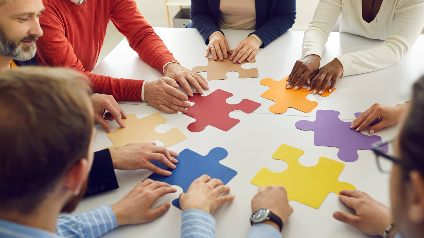 A diverse group of people assembling colorful puzzle pieces on a white table.