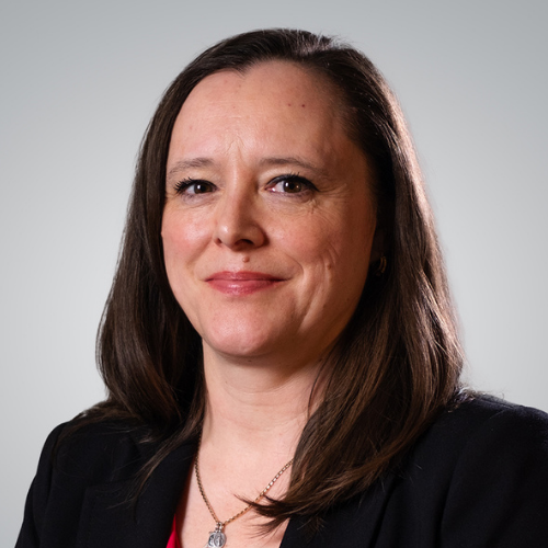 Professional woman with shoulder-length brown hair wearing a black blazer and a necklace, smiling at the camera.