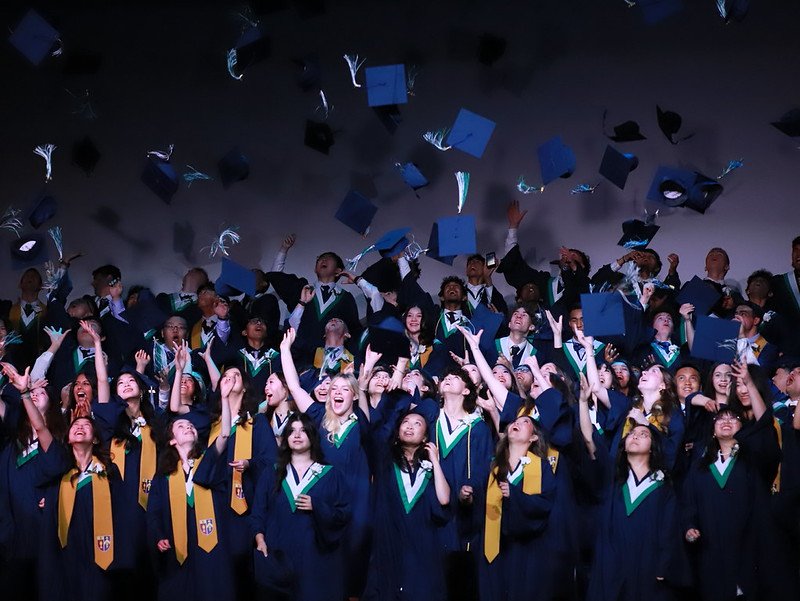 Group of graduates in caps and gowns celebrating at graduation ceremony, tossing hats in the air.