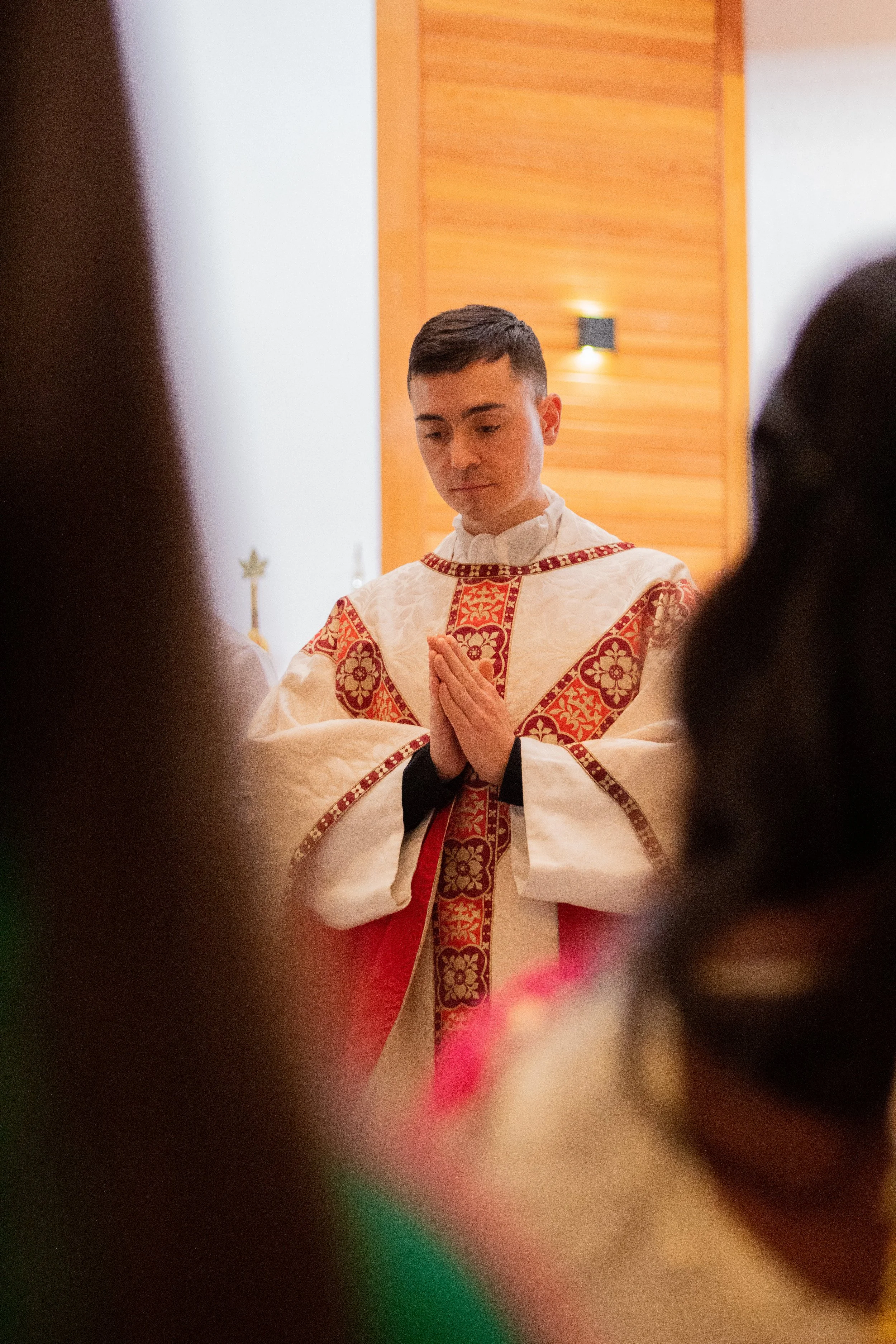 Priest in ceremonial robe, hands clasped in prayer, during a church service.
