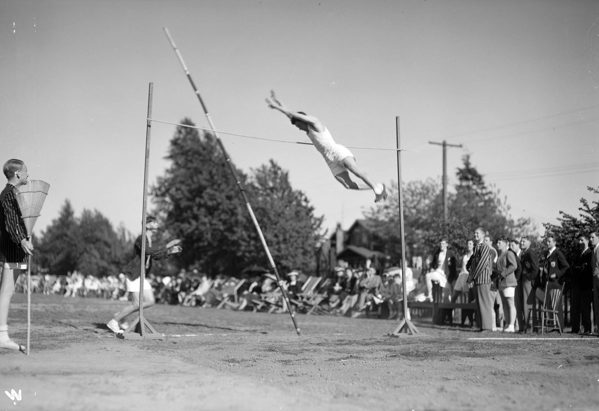 A man in mid-air during a high jump event at a track and field meet, with spectators watching.