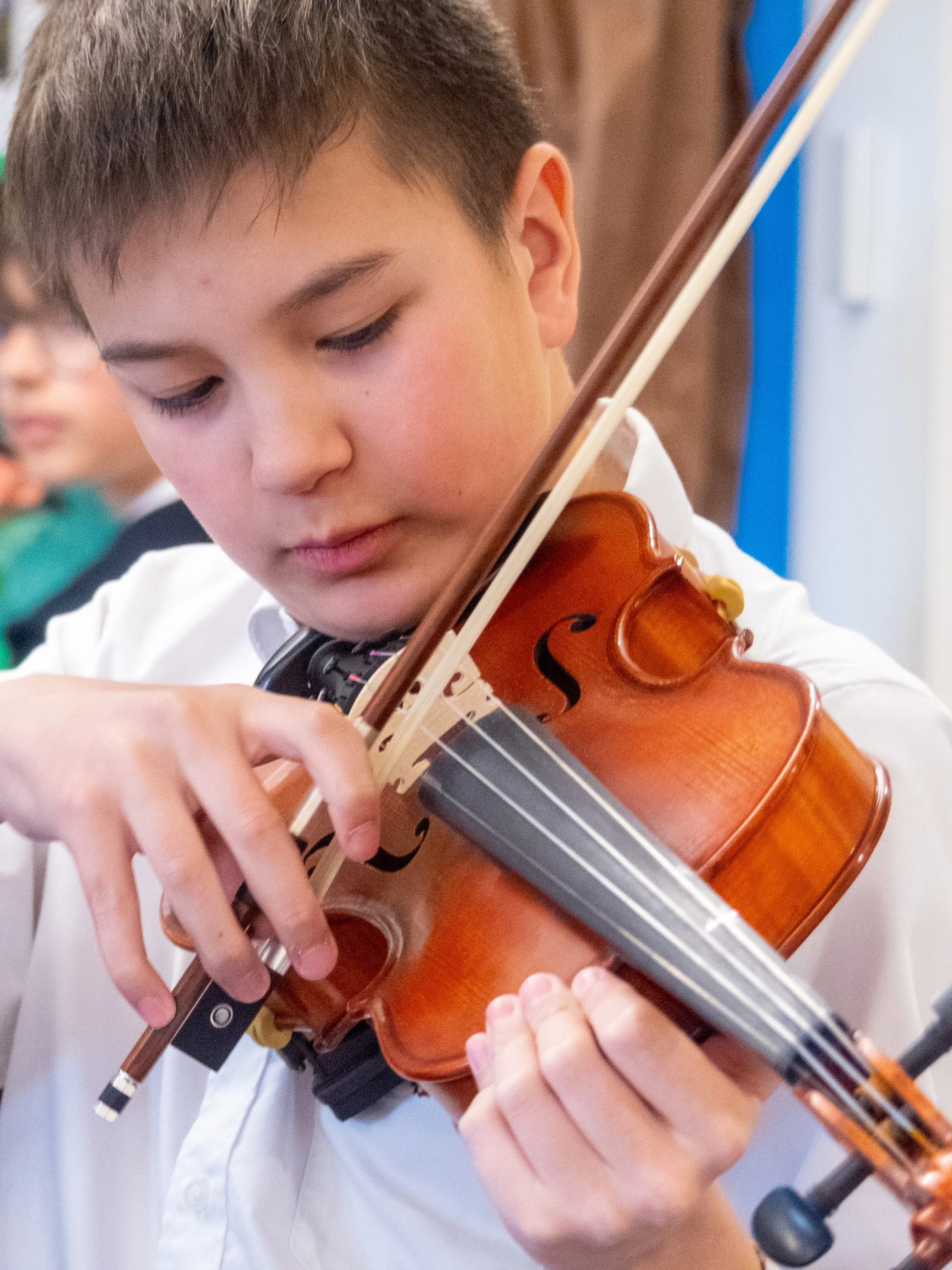 A young boy playing a violin in a classroom setting.