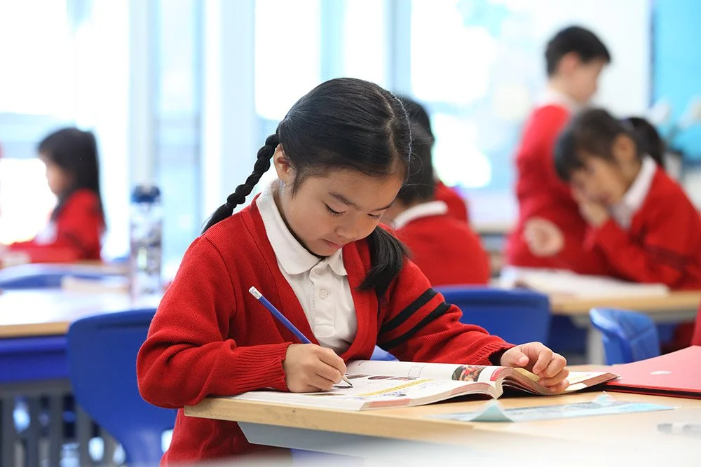 Young girl in red uniform writing in a classroom