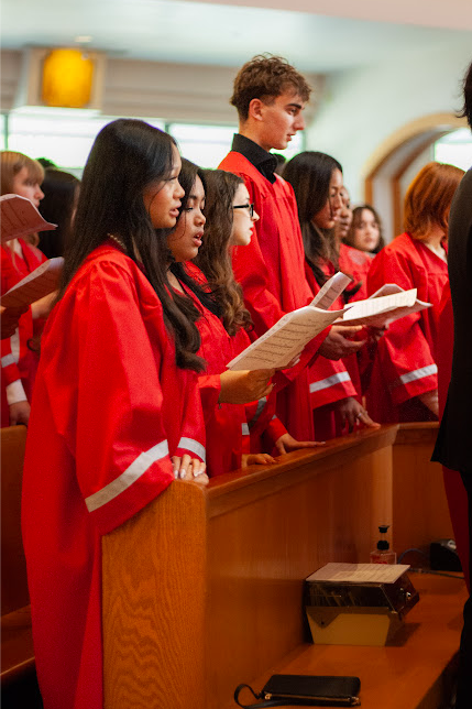 Group of young people in red robes singing or reading during a ceremony in a church.