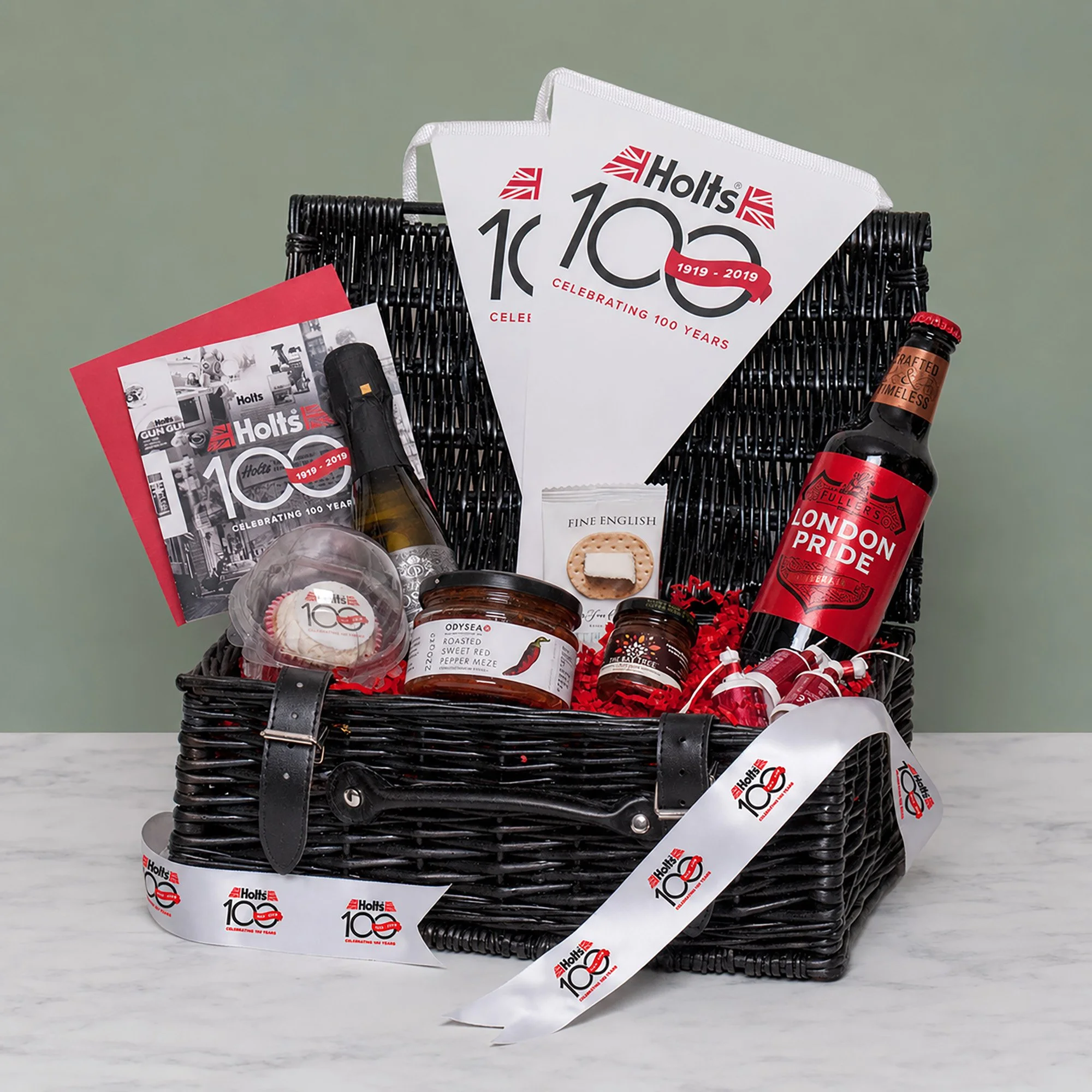 Black Wicker Basket tied with branded ribbon containing Branded card, bunting & cupcake, food items and drinks
