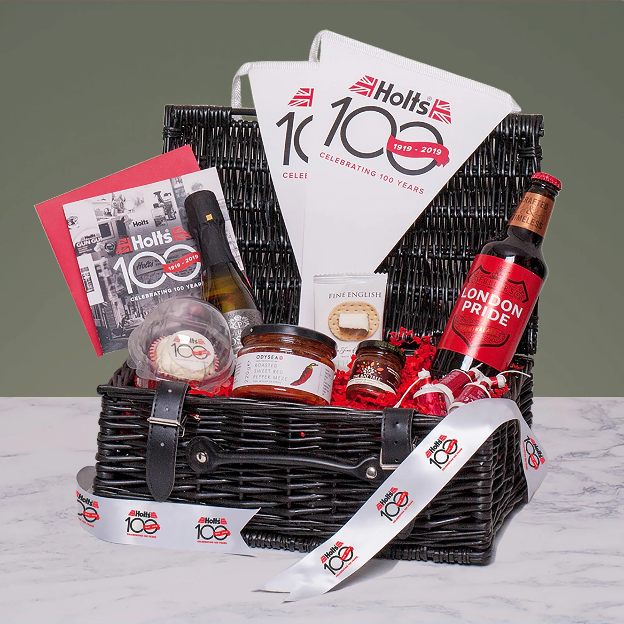 Black Wicker Basket tied with branded ribbon containing Branded card, bunting & cupcake, food items and drinks