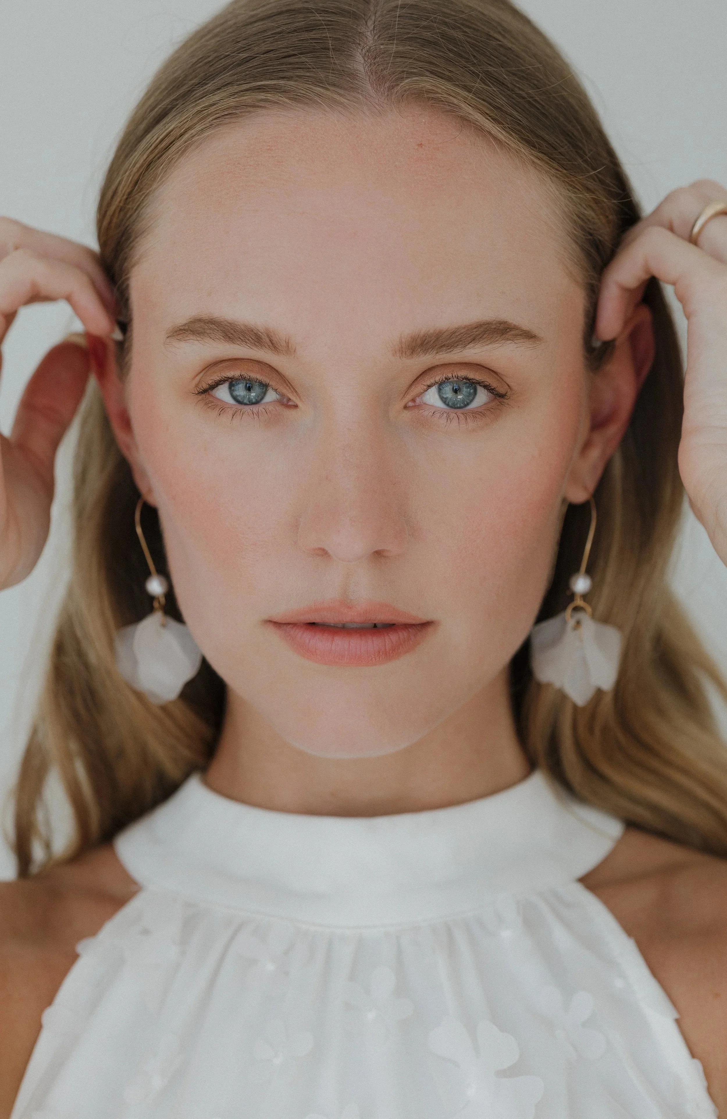 Closeup photo of blonde woman's face in white dress with blue eyes.
