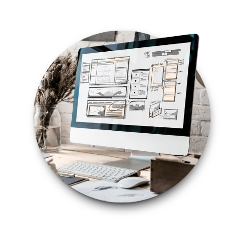 Computer monitor displaying website wireframes, on a desk with a keyboard, mouse, and other office items.