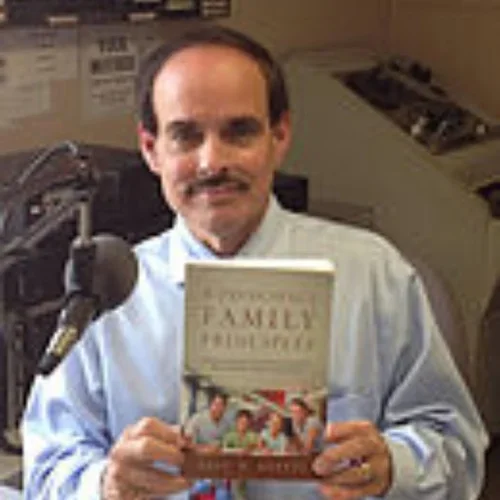 Man holding a book titled "Family Principles" in a recording studio with a microphone in the background.