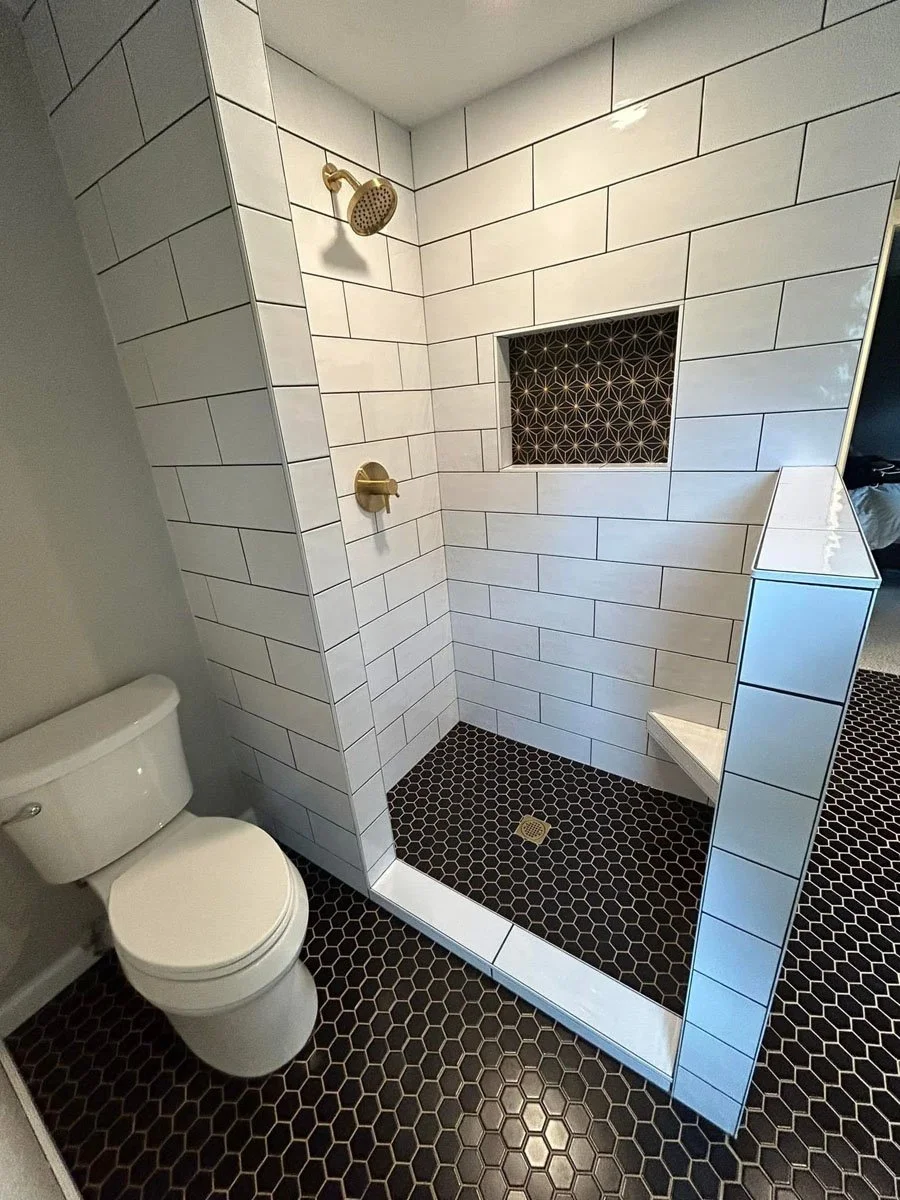 Bathroom with a white toilet next to a walk-in shower with white subway tiles and black hexagon floor tiles.