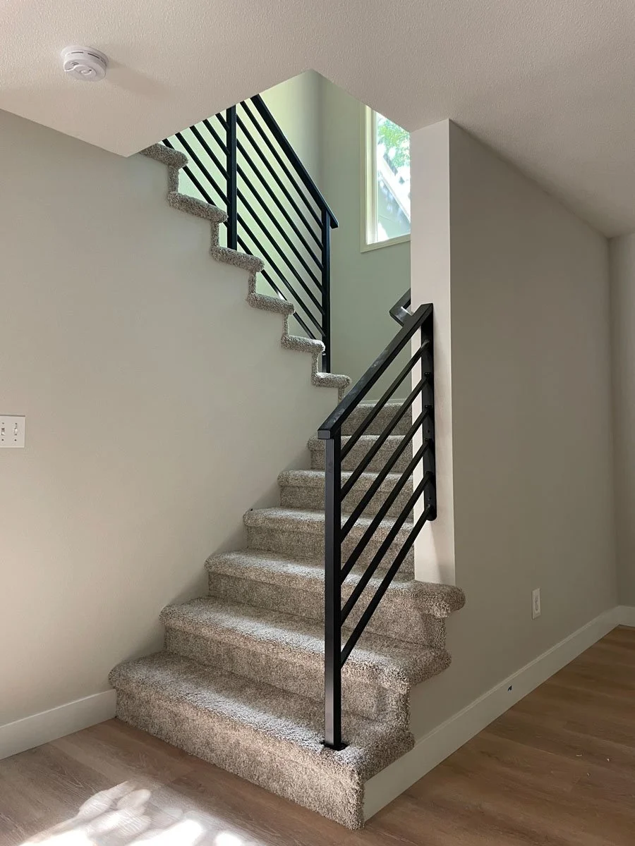 Carpeted staircase with black metal railing in a modern home, near a window.