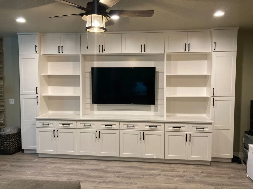 White built-in entertainment center with open shelves, cabinets, and a mounted flat-screen TV in a living room.